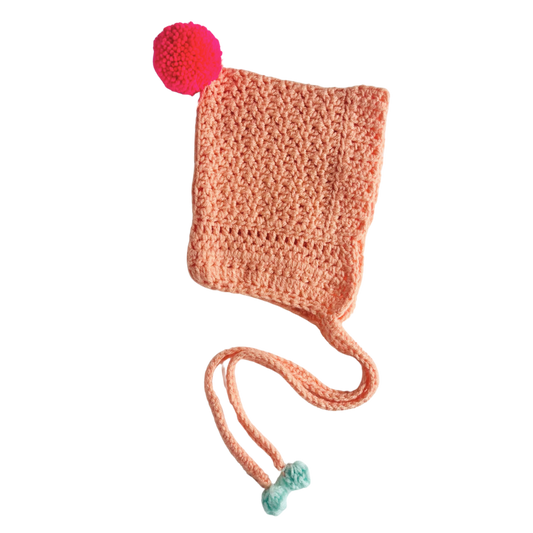 Crocheted peach-colored hat with a red pom-pom on a white background
