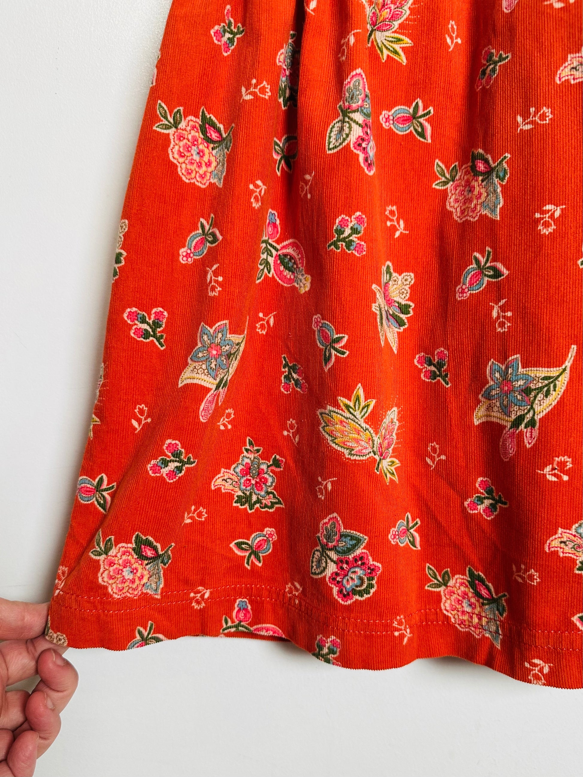 Red fabric with floral patterns held by a hand on a white background