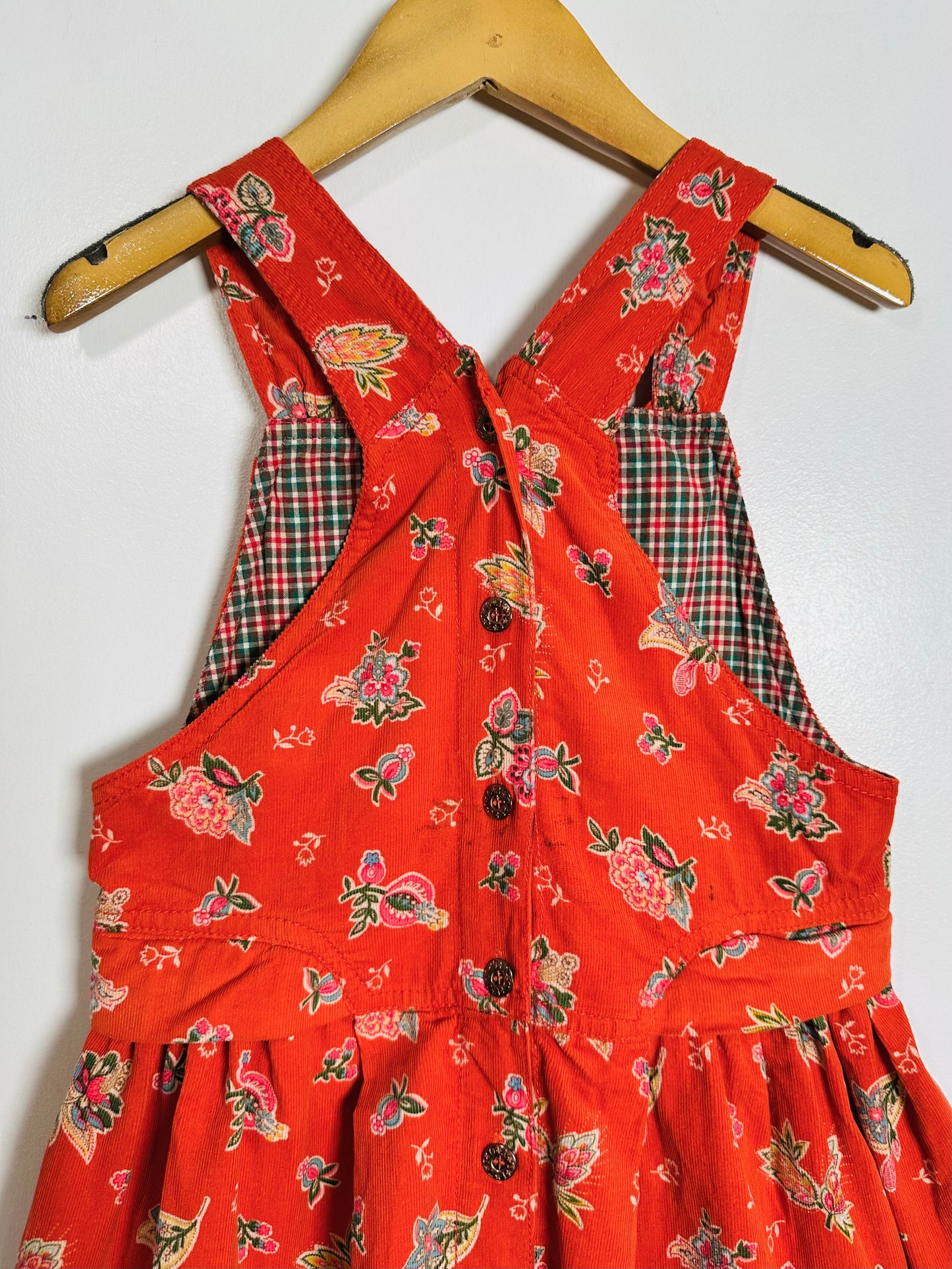 Red floral-patterned dress with plaid accents on a wooden hanger against a white background