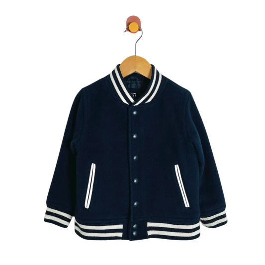 A navy blue knit varsity-style jacket with white striped trim on the collar, cuffs, and hem, hanging on a wooden hanger against a plain white background.