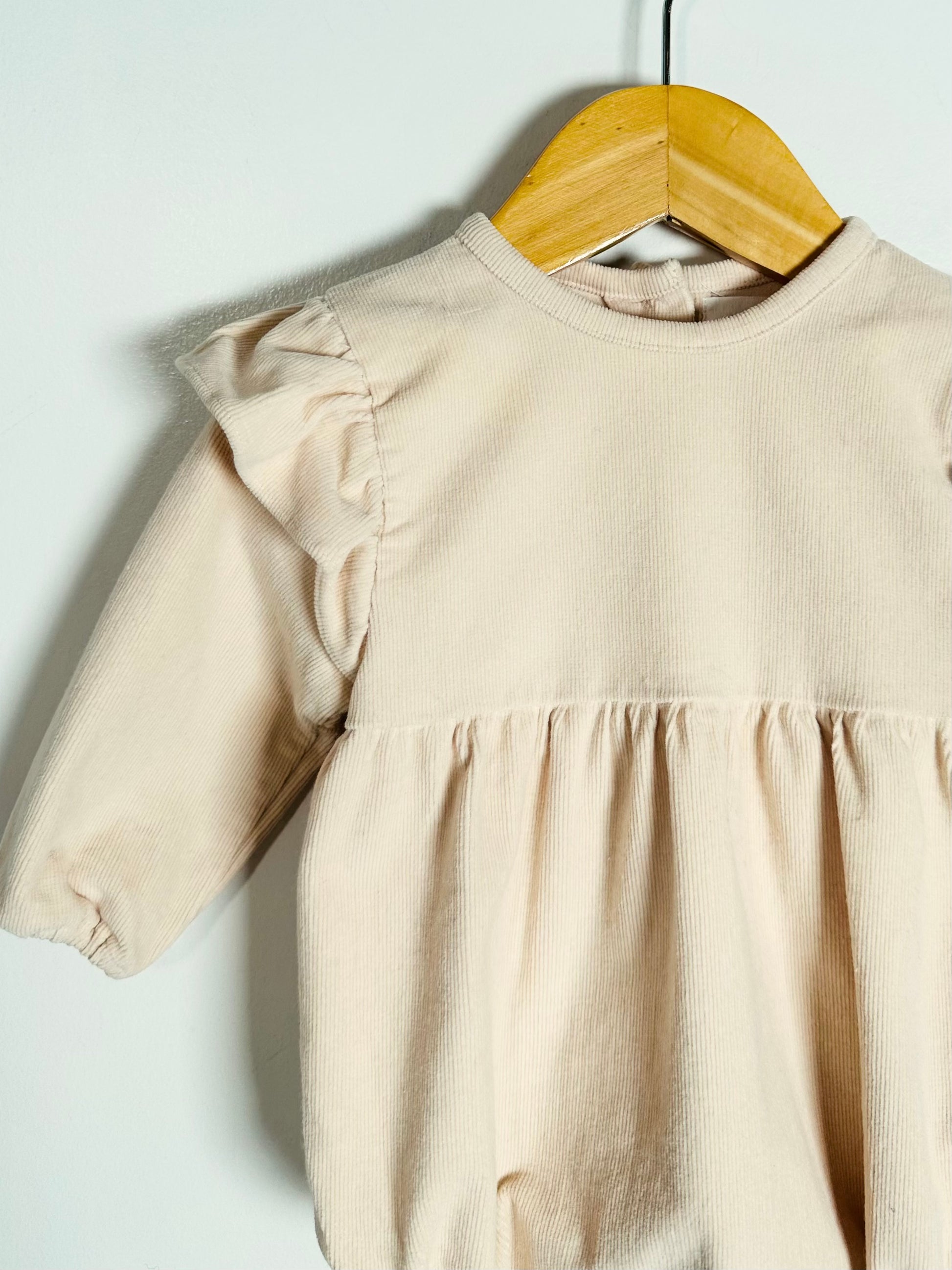 Beige baby dress on a wooden hanger against a white background
