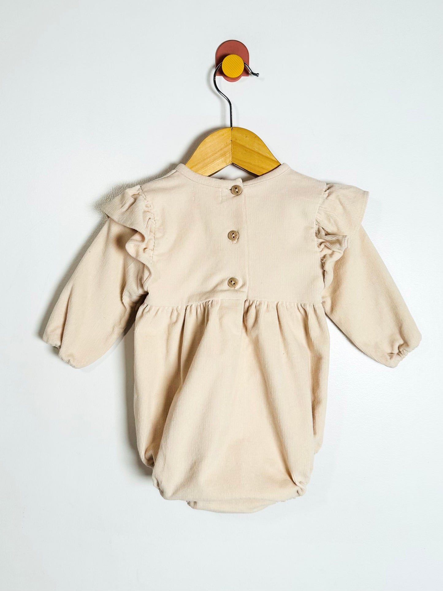Beige baby romper with ruffled sleeves on a hanger against a white background