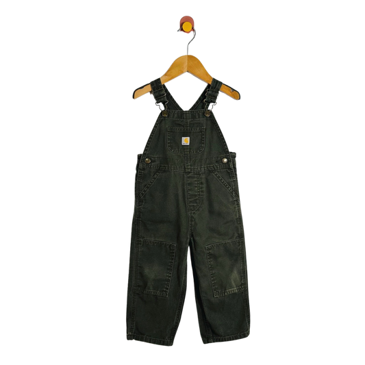 A pair of dark green denim baby overalls hanging on a wooden hanger with a red and yellow hook against a plain white background.