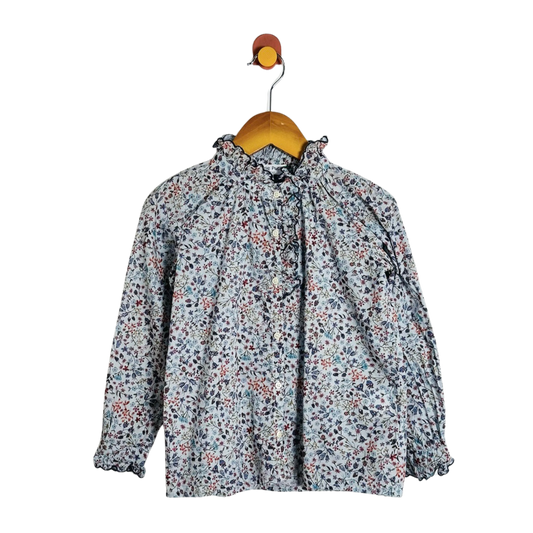 A long-sleeve blouse with a dense small floral print in muted blue, red, and black on a light gray base, hanging on a wooden hanger against a plain white background.