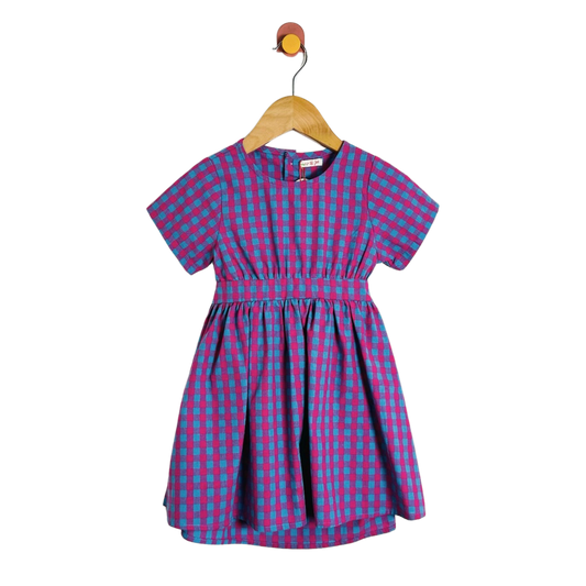 A short-sleeve children's dress with a blue and magenta gingham pattern, hanging on a wooden hanger against a plain white background.