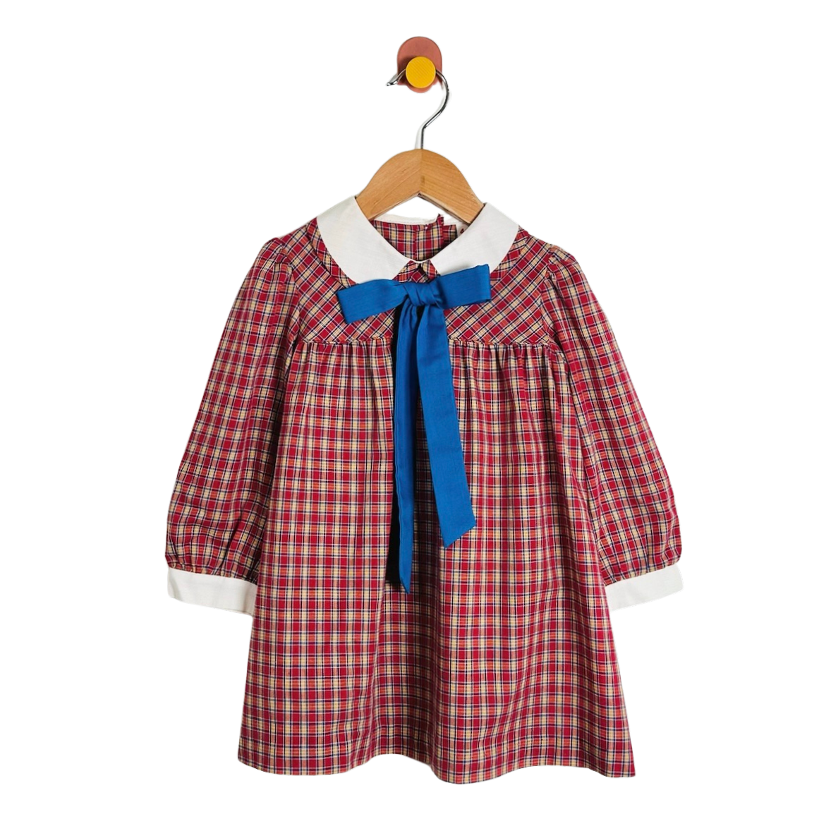 A toddler girl's long-sleeve plaid dress with a white collar and a bright blue bow at the neck, hanging on a wooden hanger against a plain white background.
