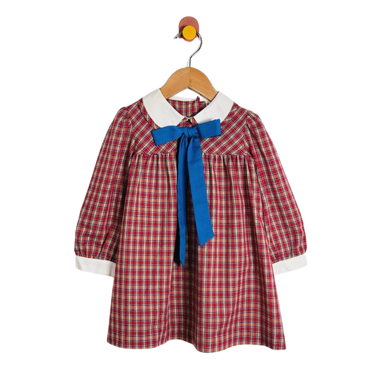 A toddler girl's long-sleeve plaid dress with a white collar and a bright blue bow at the neck, hanging on a wooden hanger against a plain white background.