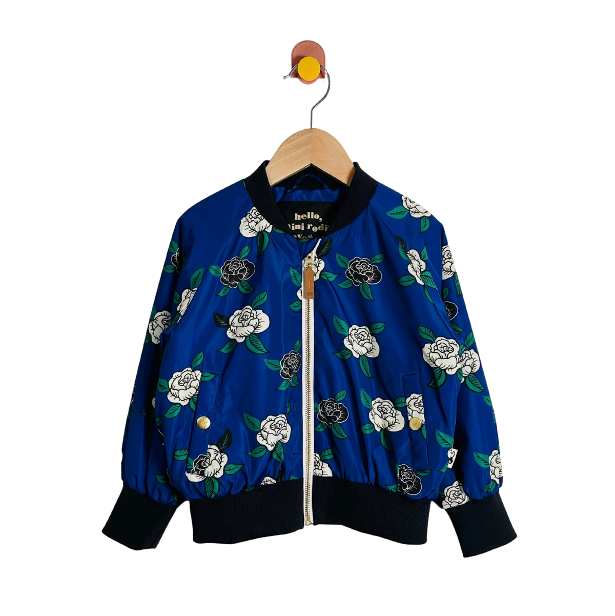 A blue bomber jacket with a white and black floral print, hanging on a wooden hanger against a plain white background.