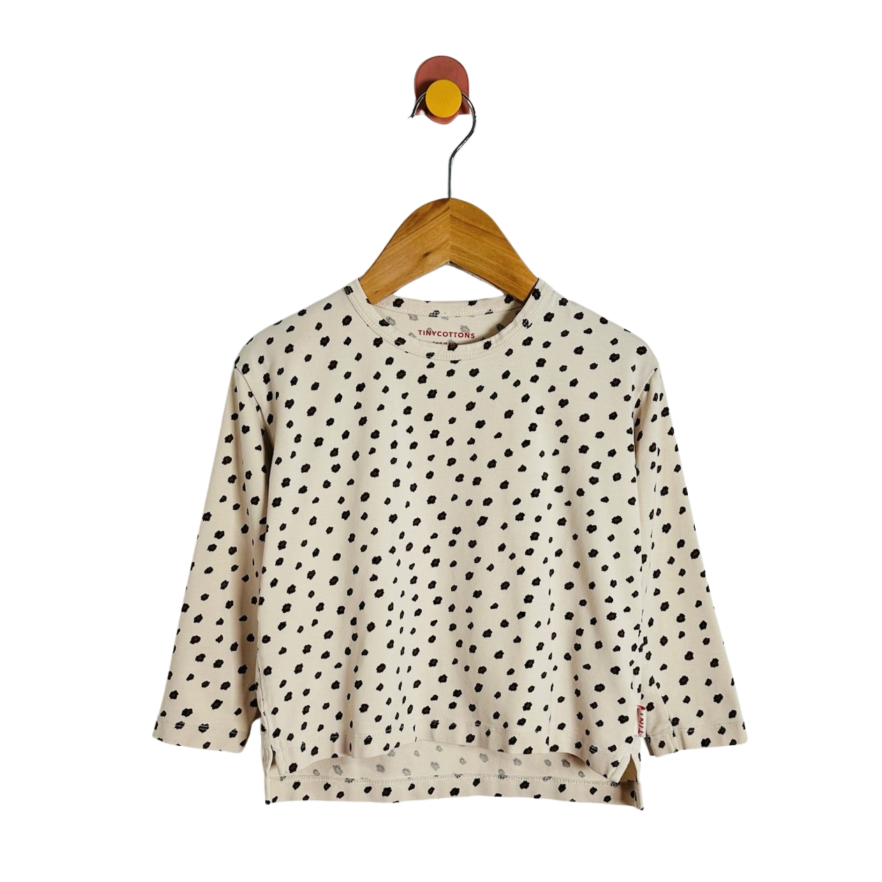 A cream-colored long-sleeve top with black polka dots, hanging on a wooden hanger against a plain white background.