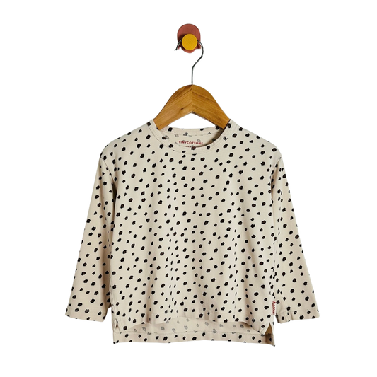 A cream-colored long-sleeve top with black polka dots, hanging on a wooden hanger against a plain white background.