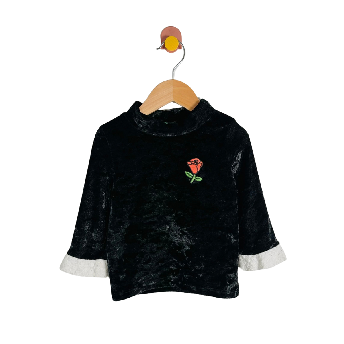 A black velvet long-sleeve top with a mock neck, featuring a small embroidered red rose on the chest and contrasting white cuffs, hanging on a wooden hanger against a white background.