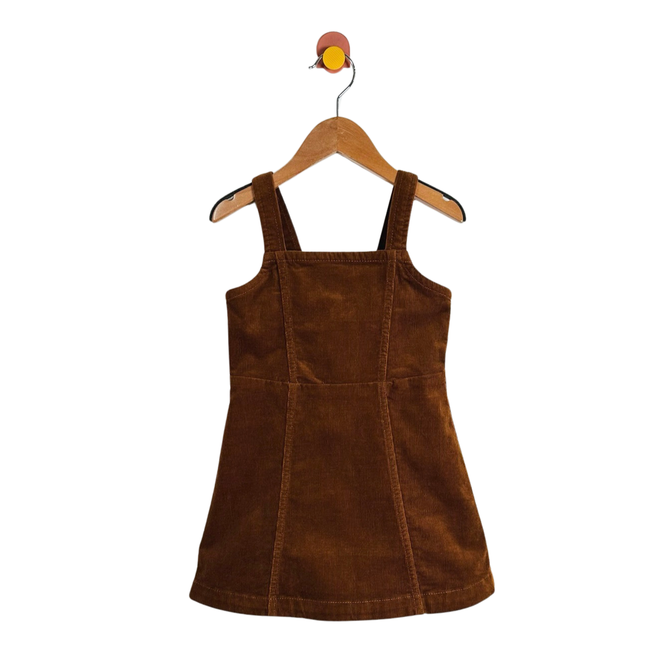 A brown corduroy pinafore dress with wide shoulder straps, hanging on a wooden hanger against a plain white background.