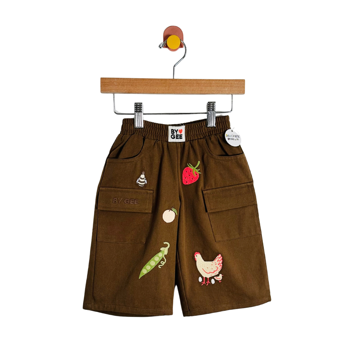 Brown corduroy shorts with embroidered vegetable and animal motifs, hanging on a wooden hanger against a white background.