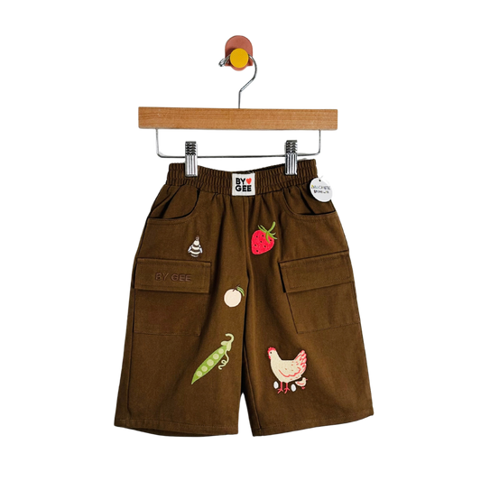 Brown corduroy shorts with embroidered vegetable and animal motifs, hanging on a wooden hanger against a white background.