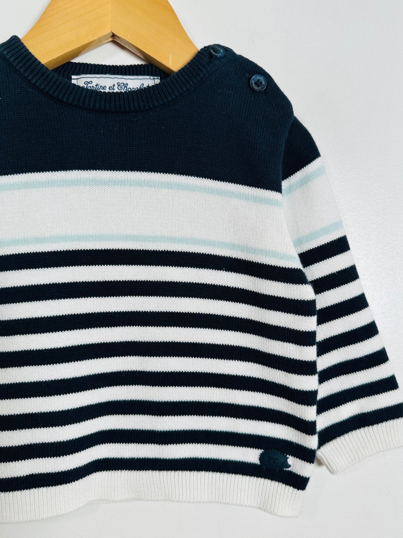 A close-up of a baby knit sweater with horizontal navy and white stripes, hanging on a wooden hanger against a plain white background.