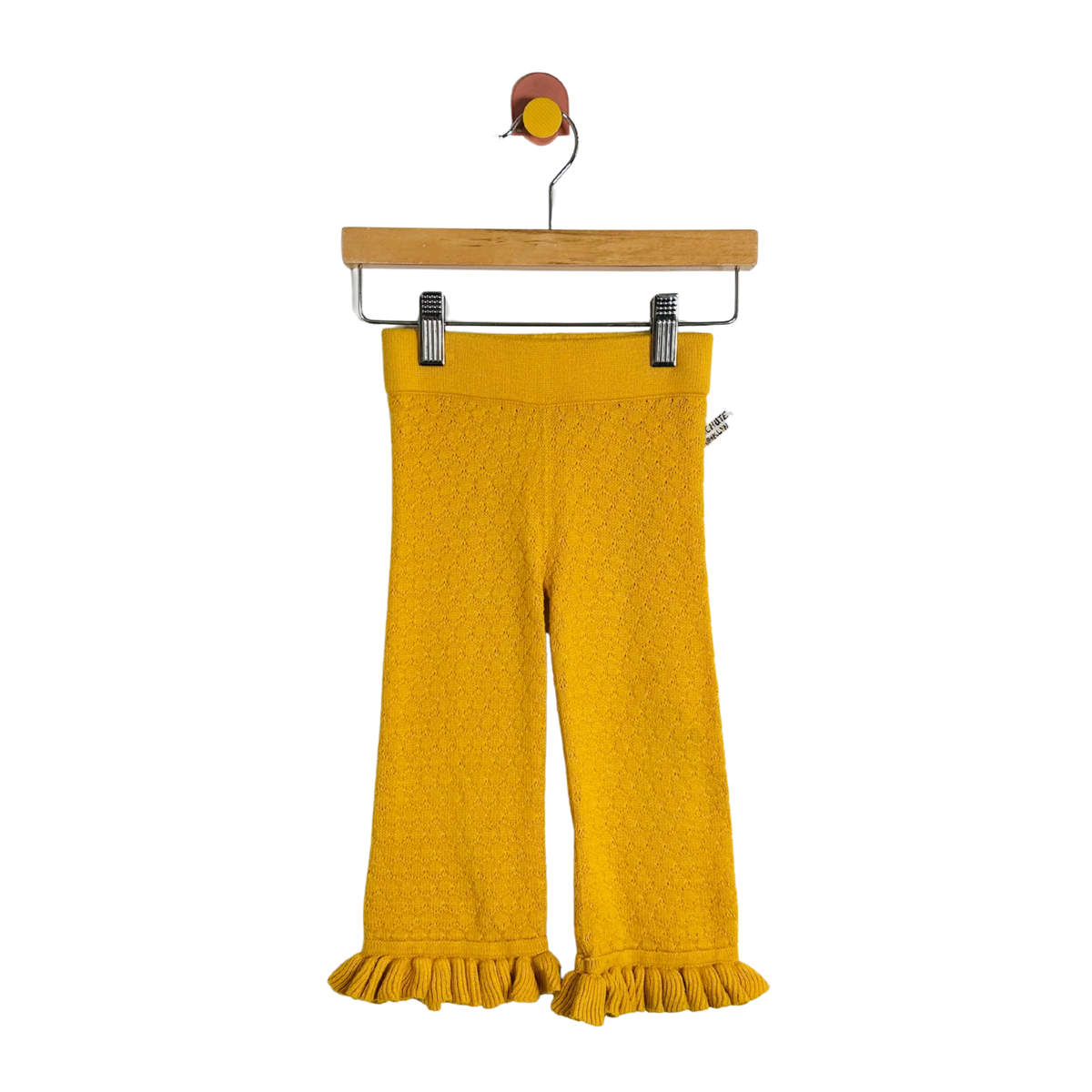 Yellow textured knit cropped pants with a ruffled hem, hanging from a wooden hanger with metal clips against a plain white background.
