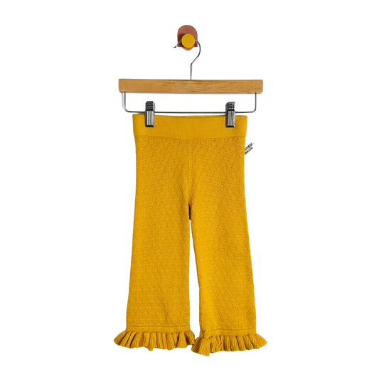 Yellow textured knit cropped pants with a ruffled hem, hanging from a wooden hanger with metal clips against a plain white background.