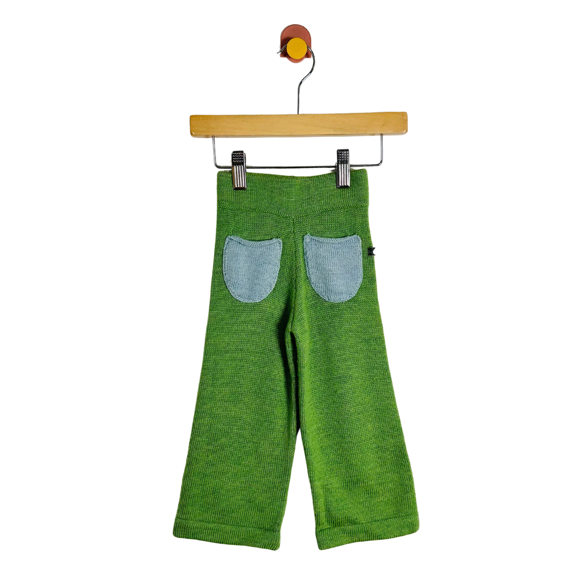Green knit pants for toddlers, shown from the back with two light blue denim patch pockets, hanging from a wooden hanger on a white background.