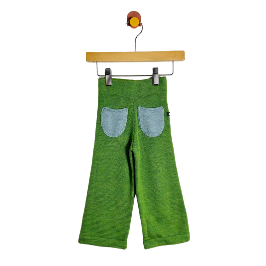 Green knit pants for toddlers, shown from the back with two light blue denim patch pockets, hanging from a wooden hanger on a white background.