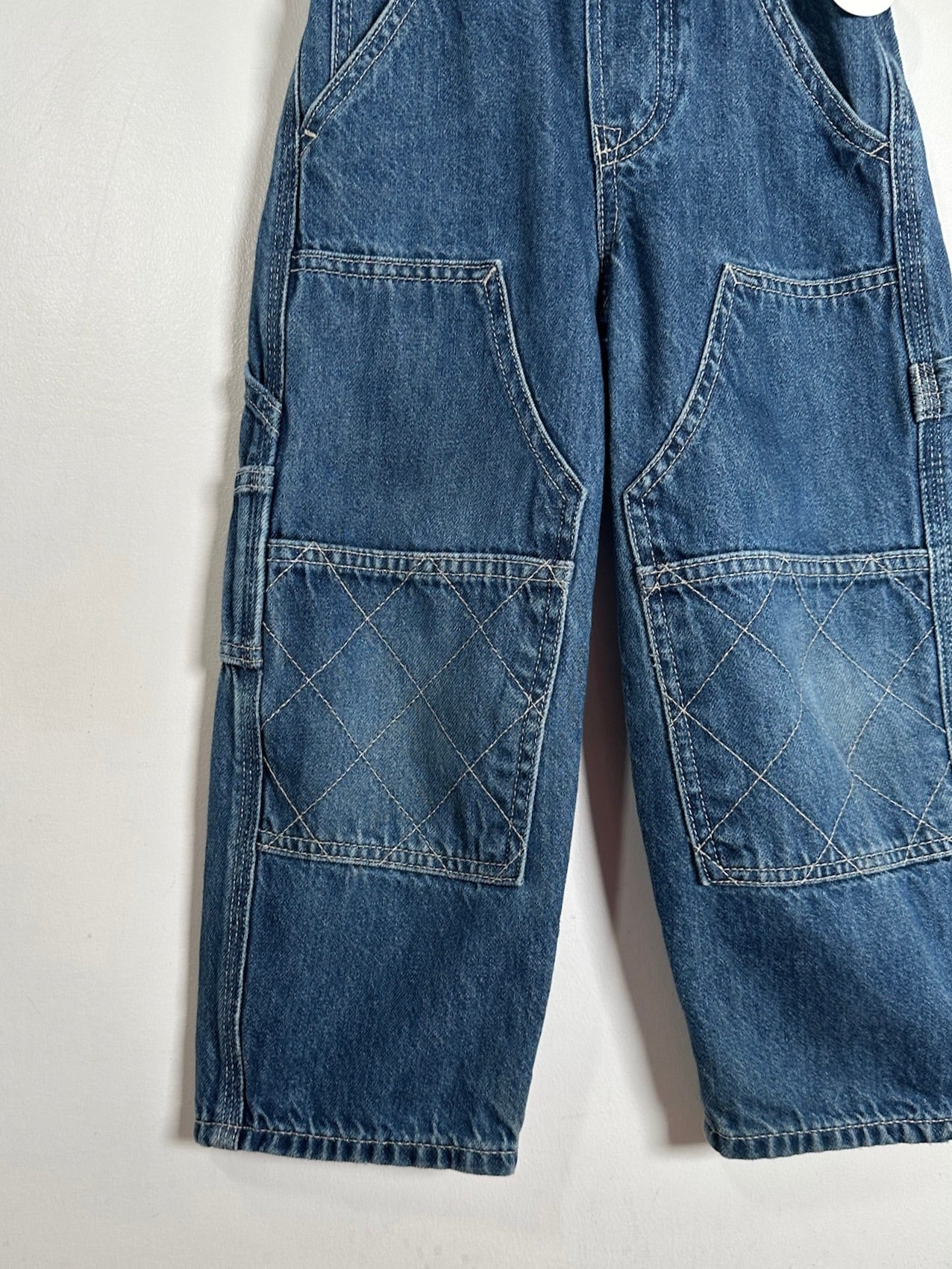Blue denim cargo pants with large front patch pockets featuring diagonal stitching, photographed against a plain off-white background.