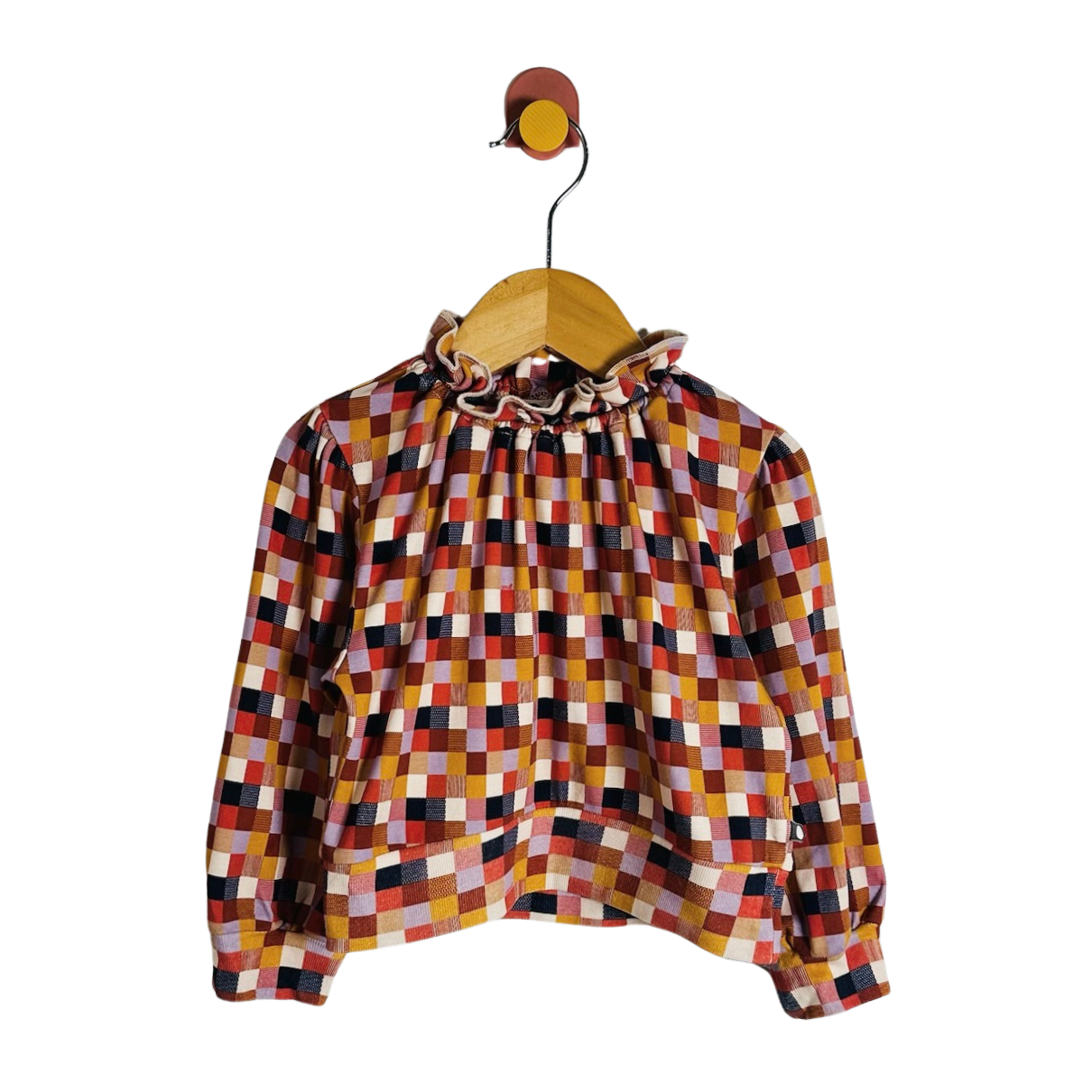 A long-sleeve blouse with a colorful geometric checkered pattern, featuring a ruffled high neck and gathered sleeves, hanging on a wooden hanger against a plain white background.