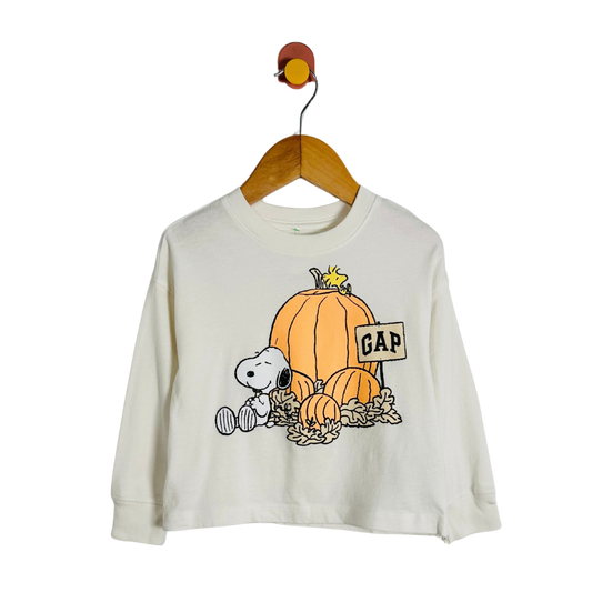 A cream-colored long-sleeve t-shirt featuring a Snoopy and Woodstock autumn graphic with pumpkins and a 'GAP' sign, hanging on a wooden hanger against a white background.
