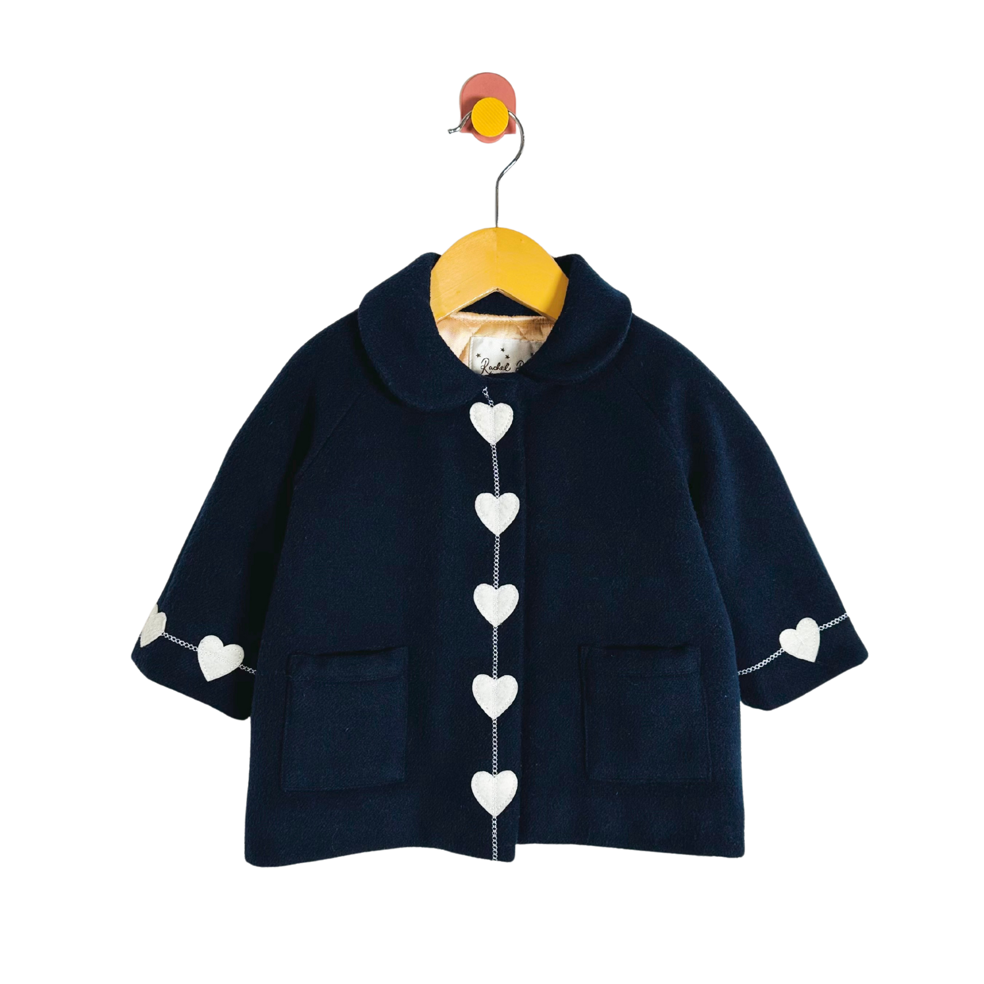 Navy blue children's coat with heart patterns on a hanger against a white background