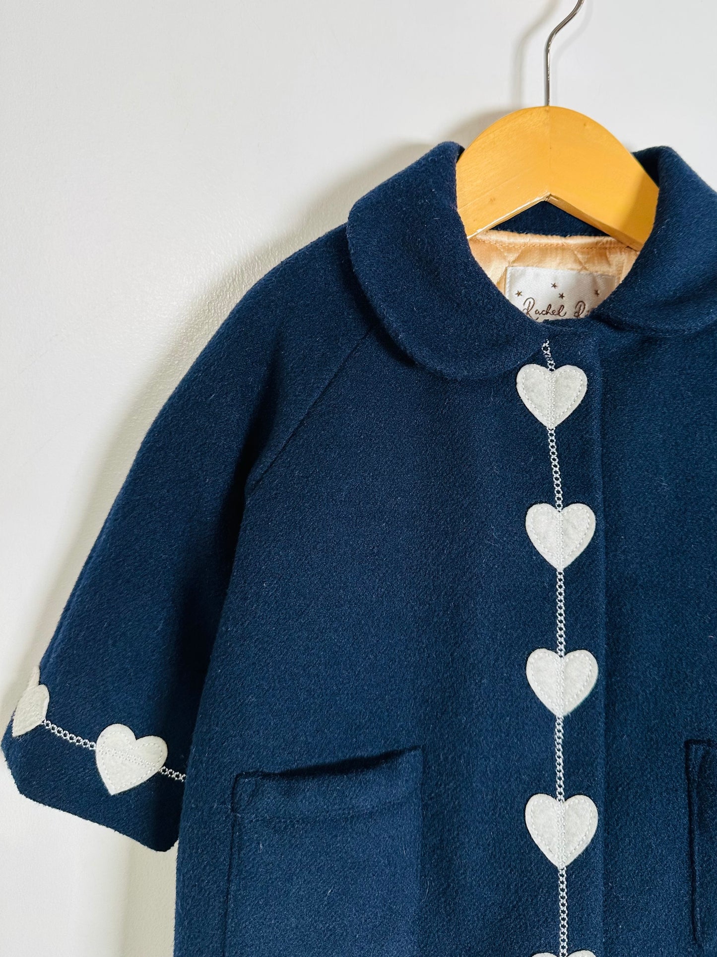 Navy blue coat with white heart patterns on a wooden hanger against a white background