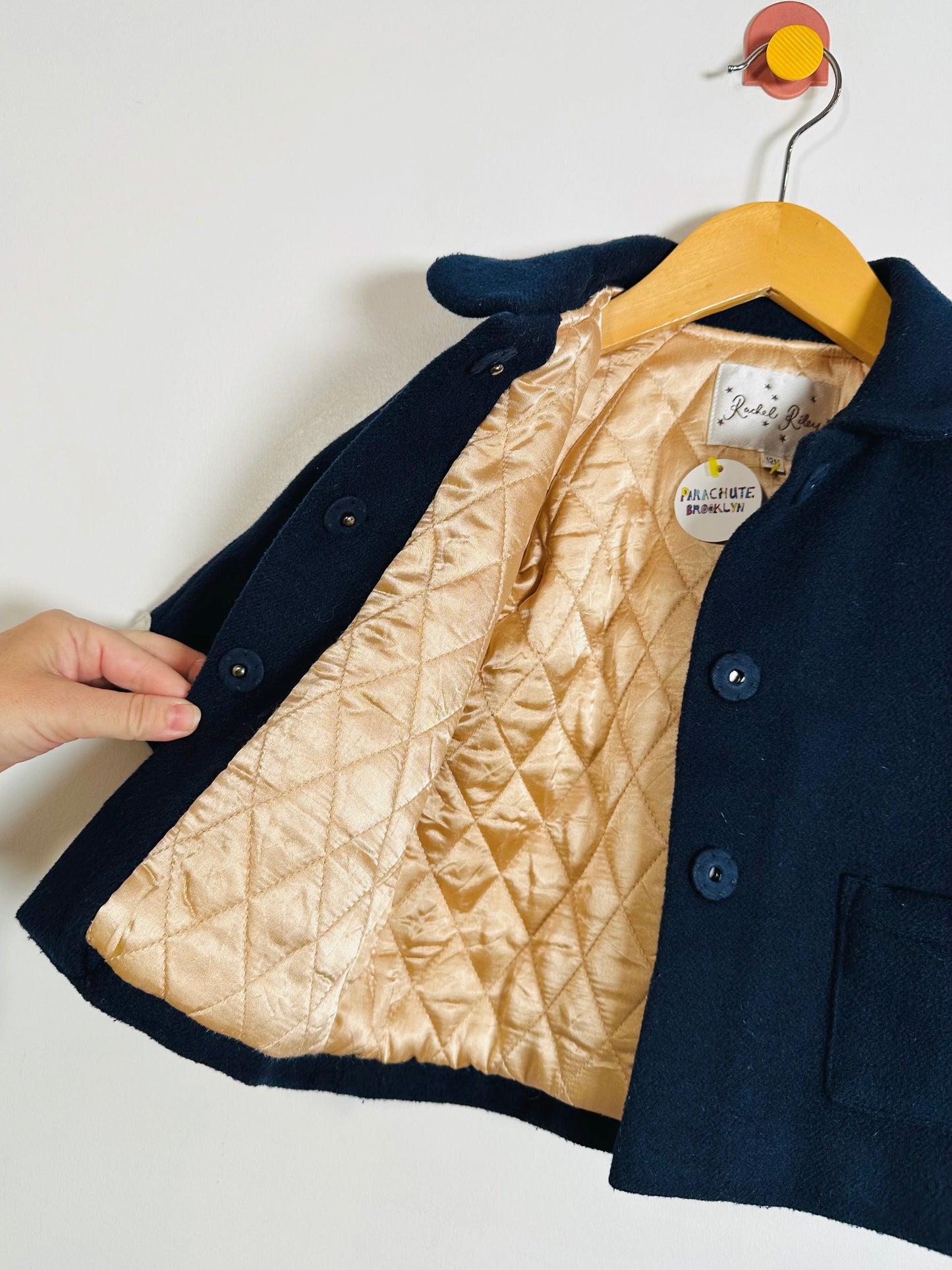Navy blue coat with beige quilted lining on a hanger against a white background