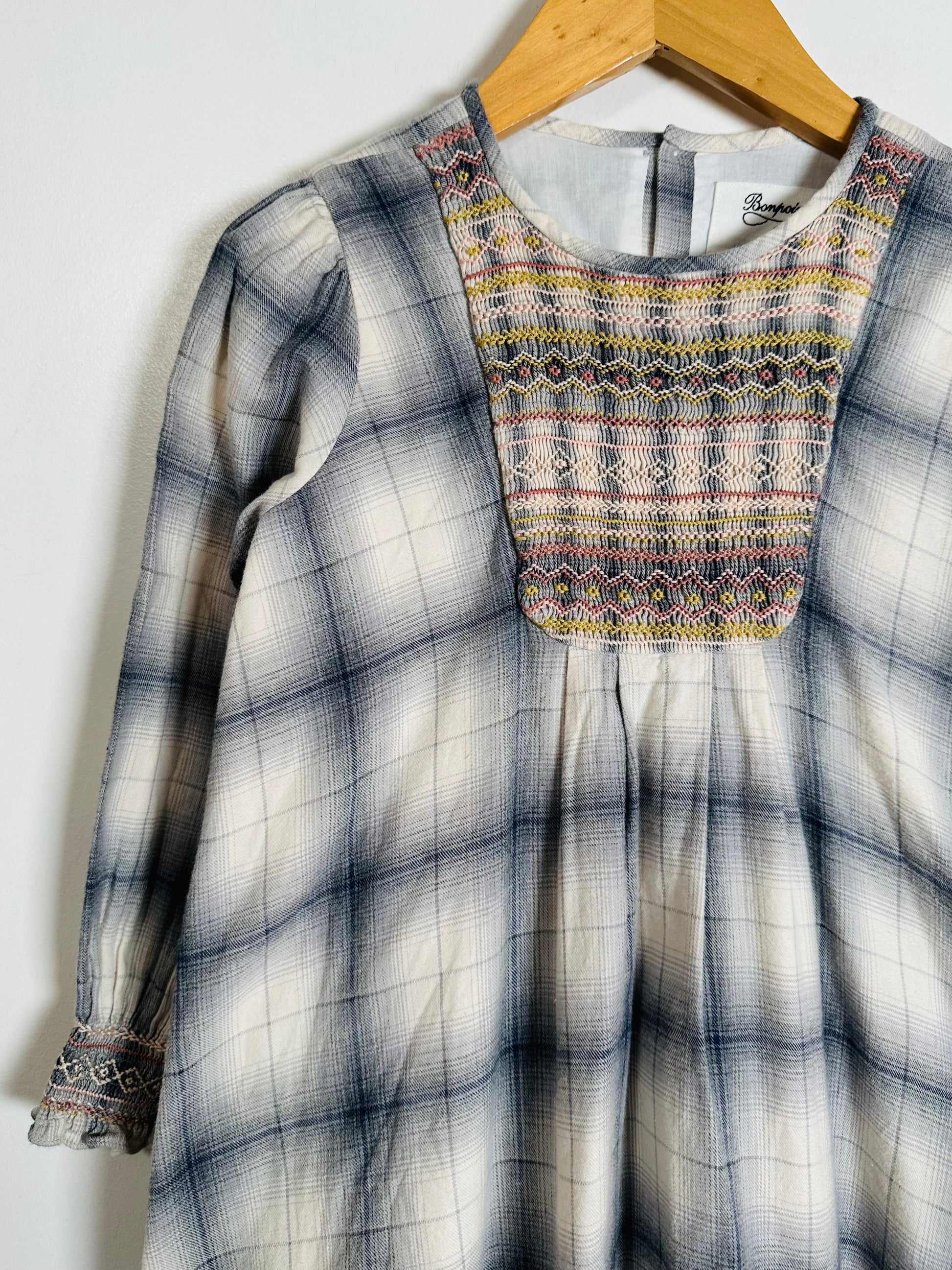 Plaid dress with embroidered neckline on a wooden hanger against a white background