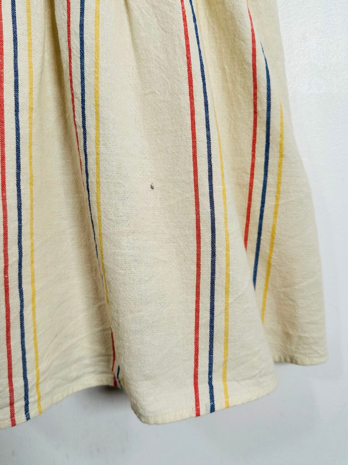 A close-up of a cream-colored fabric, likely a linen tablecloth or kitchen towel, featuring vertical stripes in red, yellow, and blue.