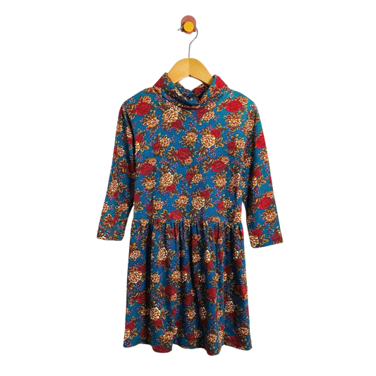 A long-sleeve cowl-neck dress with a vibrant floral print, hanging on a wooden hanger against a plain white background.