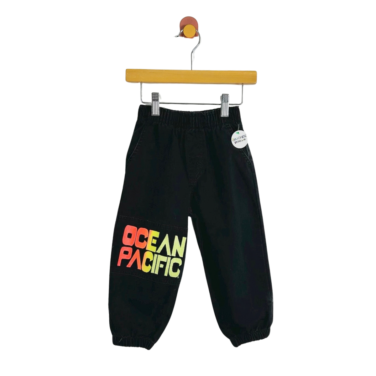 Black jogger pants with a colorful 'OCEAN PACIFIC' graphic on the left leg, hanging from a wooden hanger against a white background.