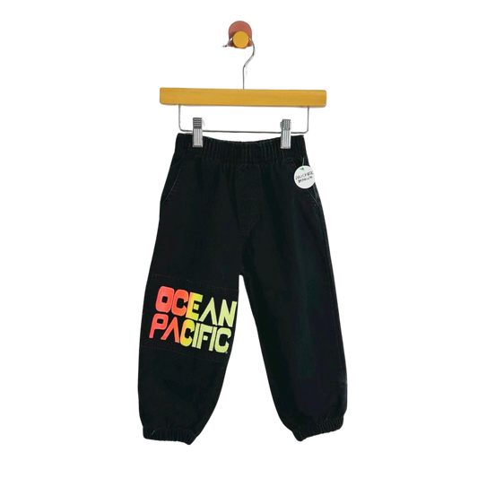 Black jogger pants with a colorful 'OCEAN PACIFIC' graphic on the left leg, hanging from a wooden hanger against a white background.