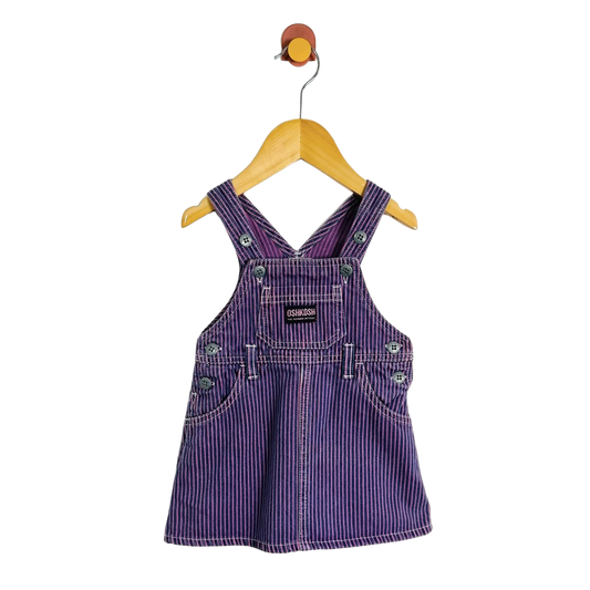 A baby/toddler purple denim overall dress with thin white vertical stripes, hanging on a wooden hanger against a plain white background.