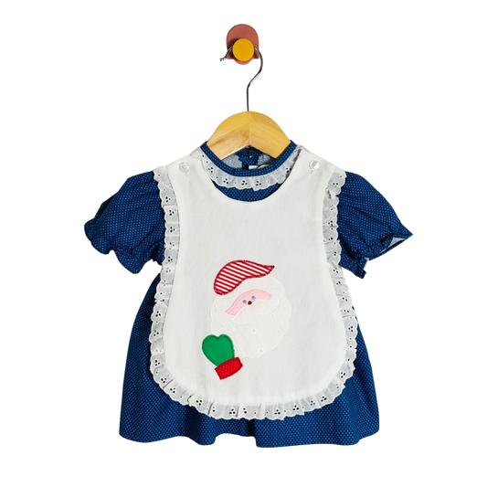 Blue dress with a white apron featuring a santa design on a hanger against a white background