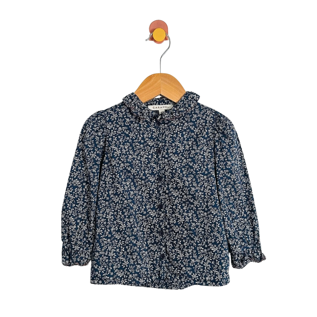 A long-sleeve button-up blouse with a dense white floral print on a dark navy blue base, hanging on a wooden hanger against a plain white background.