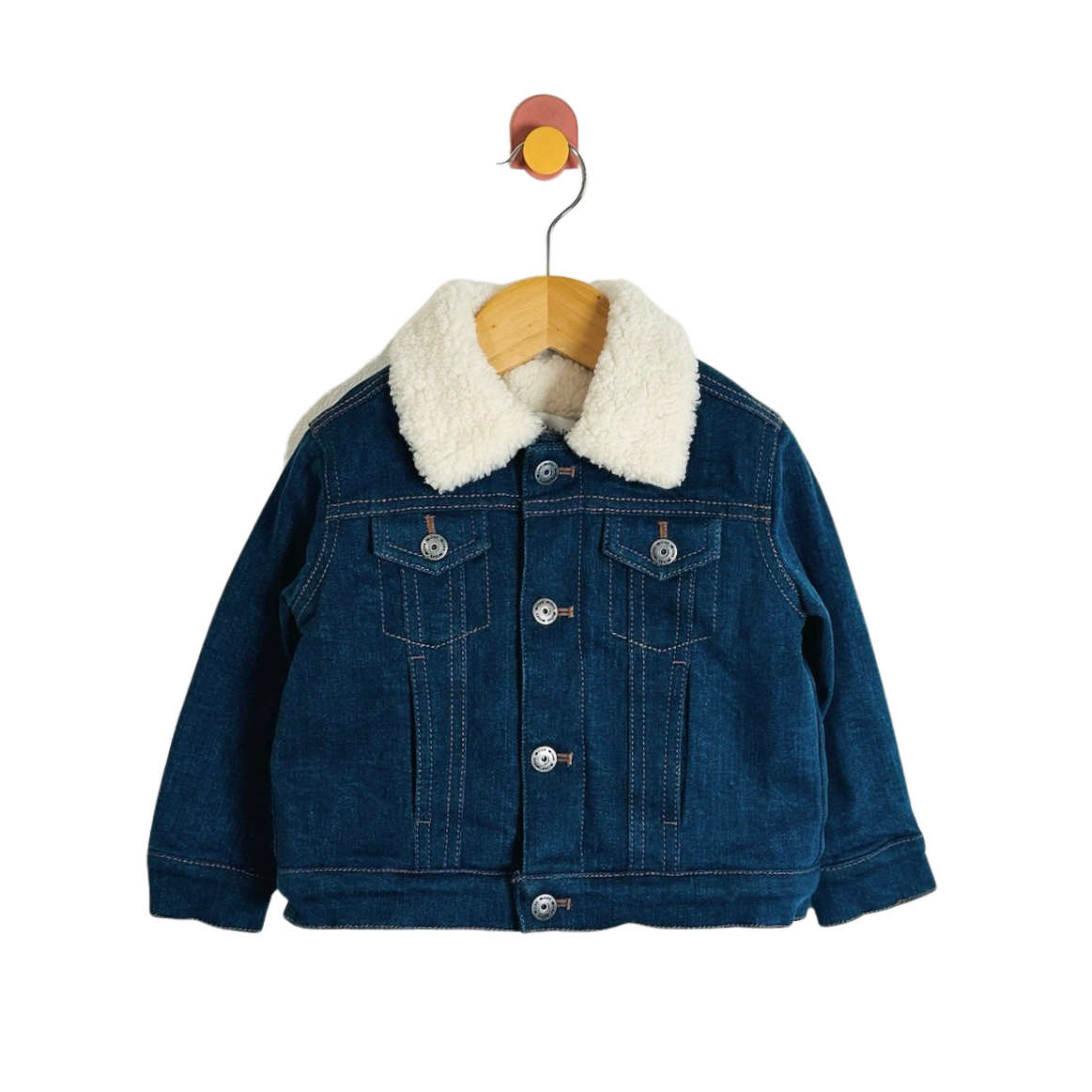 A children's dark blue denim jacket with a thick white sherpa fleece collar, hanging on a wooden hanger against a plain white background.