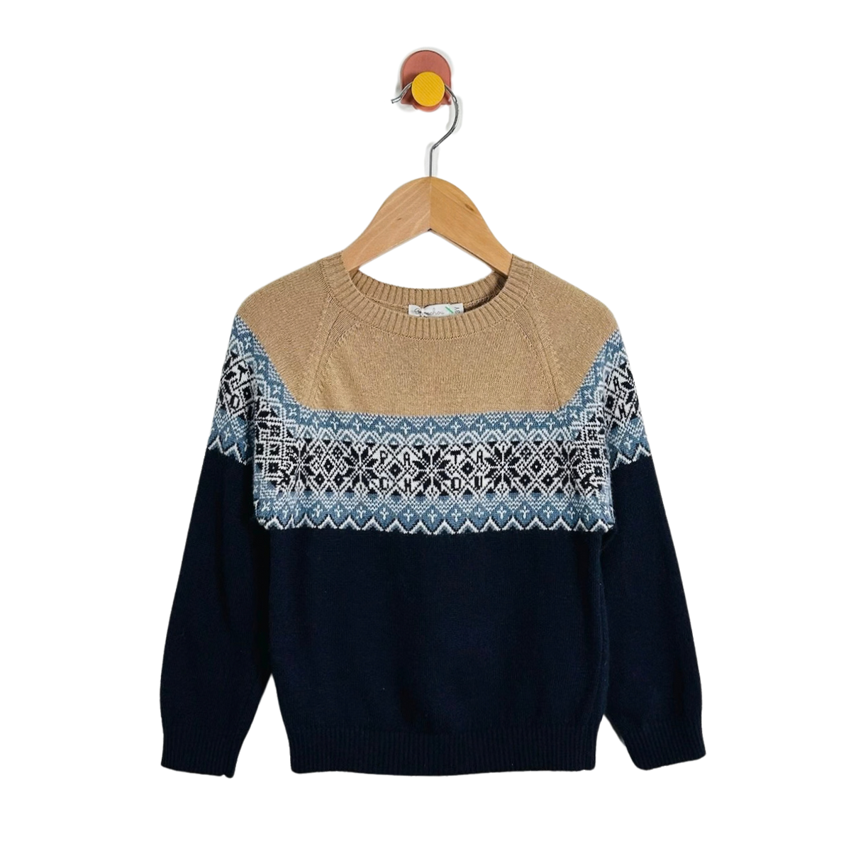 A knit crewneck sweater hanging on a wooden hanger against a plain white background. The sweater has a tan upper yoke, a horizontal Fair Isle-style pattern band in blue, white, and black, and dark navy sleeves and lower body.