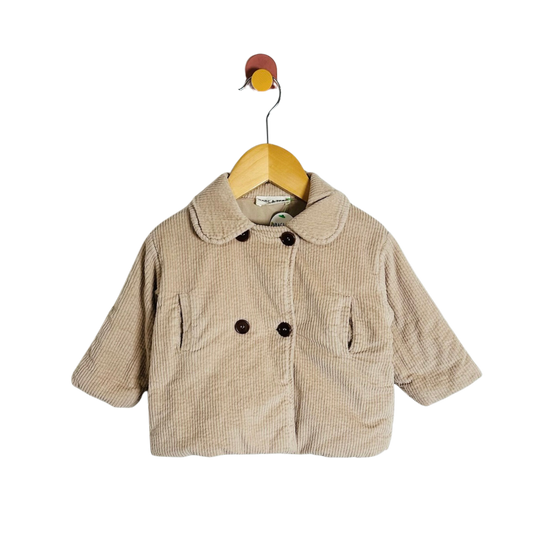 A baby's corduroy jacket in beige, featuring a Peter Pan collar, double-breasted buttons, and front patch pockets, hanging on a wooden hanger against a white background.