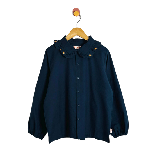 A navy blue long-sleeve button-up shirt with a ruffled Peter Pan collar decorated with small gold star appliqués, hanging on a wooden hanger against a plain white background.