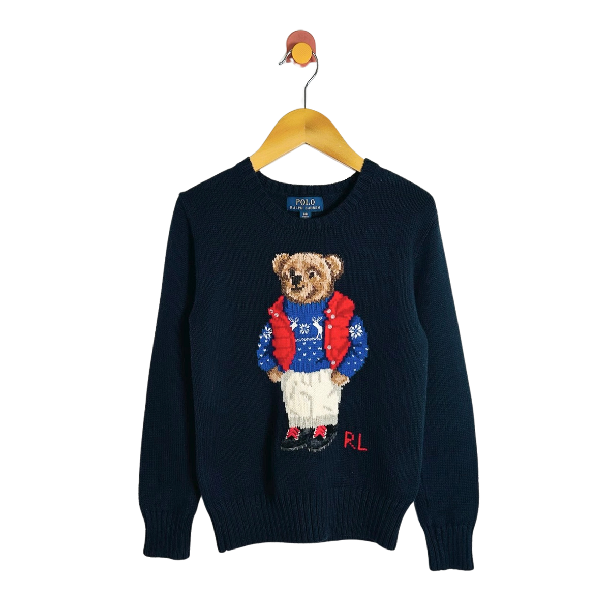 A navy blue knit sweater hanging on a wooden hanger against a white background, featuring a large embroidered teddy bear wearing a red sweater and white pants on the front, with 'RL' initials at the hem.