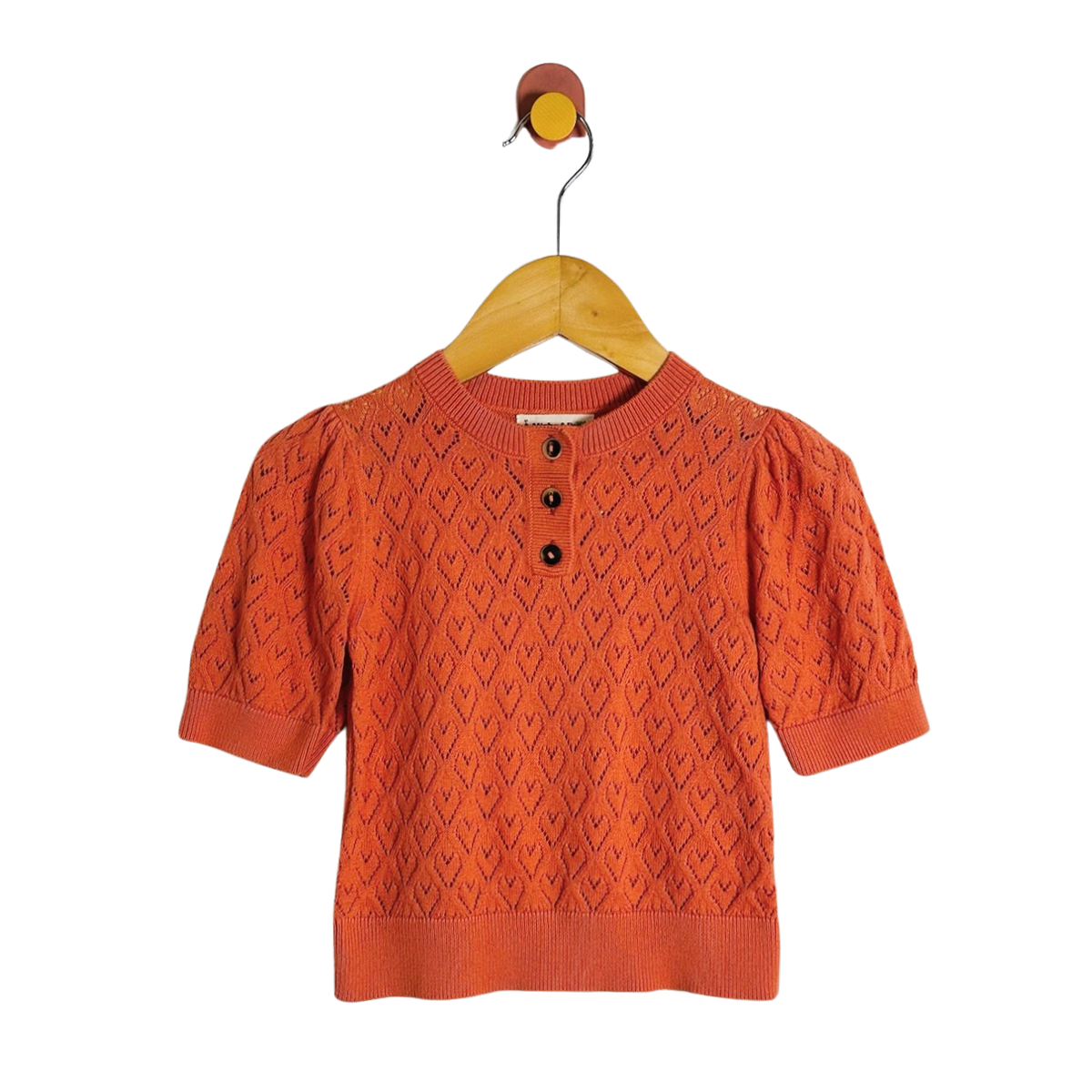 An orange short-sleeve knit top with a textured geometric pattern and three black buttons at the collar, hanging on a wooden hanger against a white background.