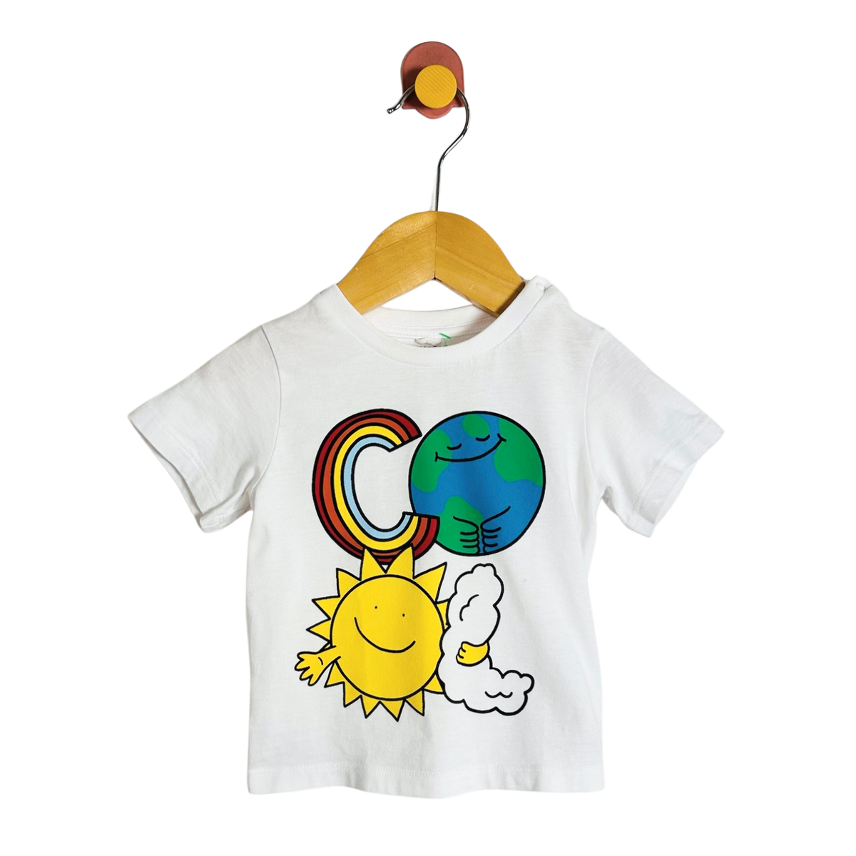 A white short-sleeve baby T-shirt hanging on a wooden hanger against a plain white background. The shirt features a colorful cartoon graphic of a rainbow, a blue and green Earth, a yellow sun, and a white cloud.