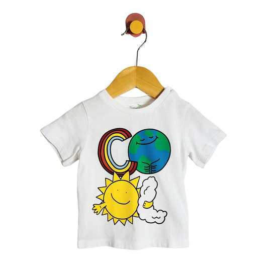 A white short-sleeve baby T-shirt hanging on a wooden hanger against a plain white background. The shirt features a colorful cartoon graphic of a rainbow, a blue and green Earth, a yellow sun, and a white cloud.