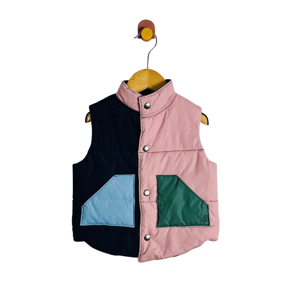 A sleeveless quilted puffer vest with a split color-block design, hanging on a wooden hanger against a white background. The left side is navy blue with a light blue triangular pocket, and the right side is light pink with a dark green triangular pocket.