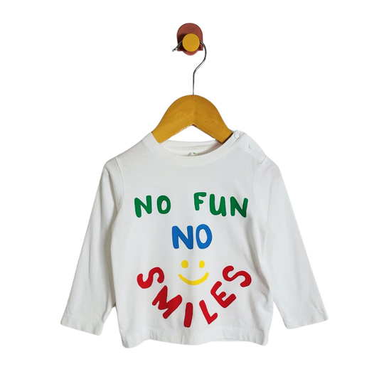 A white long-sleeve baby t-shirt with a colorful graphic reading 'NO FUN NO SMILES' and a smiley face, hanging on a wooden hanger against a white background.