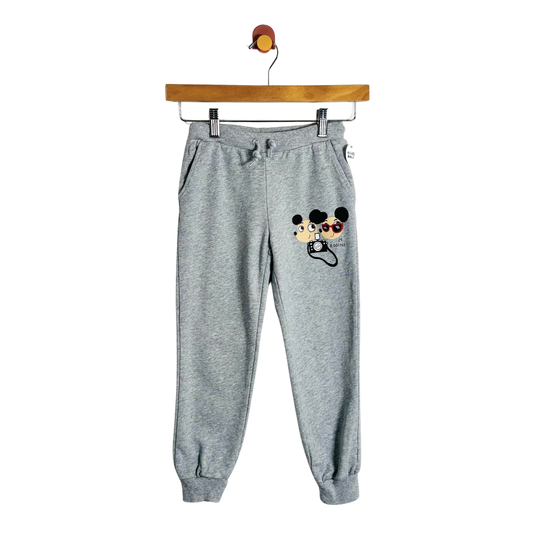 Gray heather jogger sweatpants with a Mickey Mouse and Minnie Mouse graphic on the left thigh, hanging from a wooden hanger against a white background.