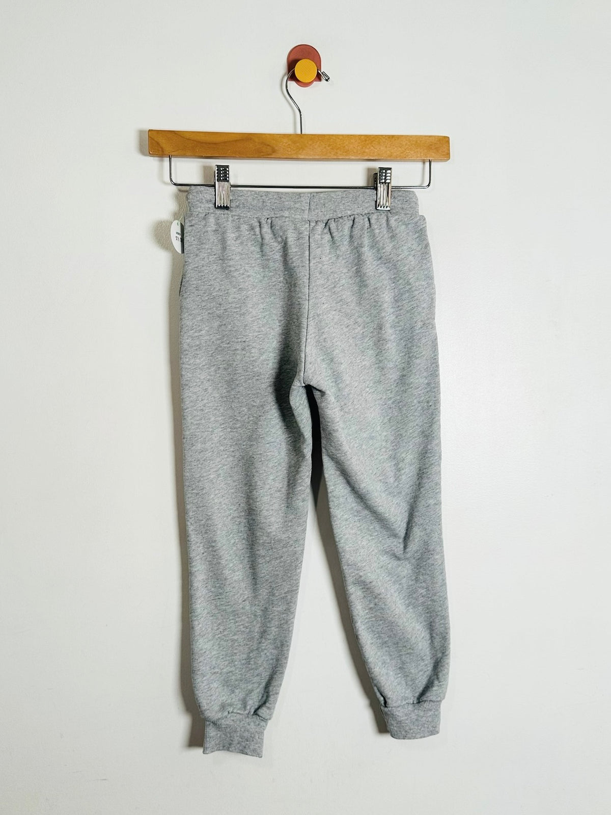 Light gray heather sweatpants hanging from a wooden hanger against a plain off-white wall.