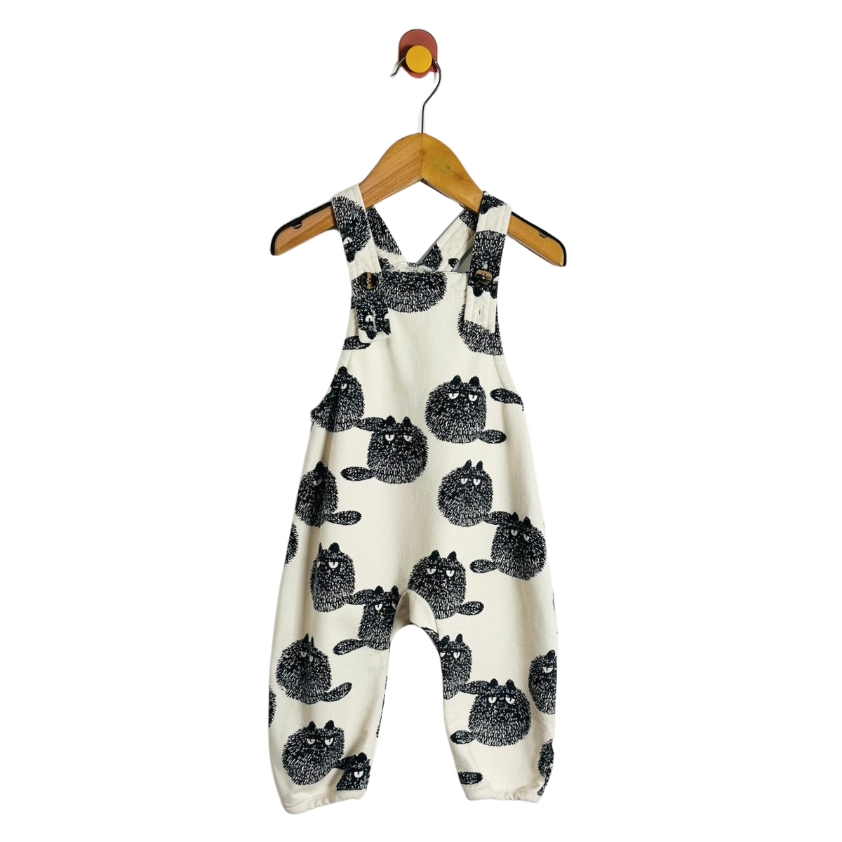 A baby romper in cream fabric with a black cat pattern, hanging on a wooden hanger against a plain white background.